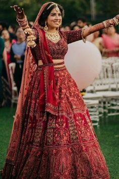 a woman in a red and gold bridal outfit is dancing with her arms outstretched