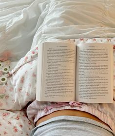 an open book laying on top of a person's stomach in bed with white sheets