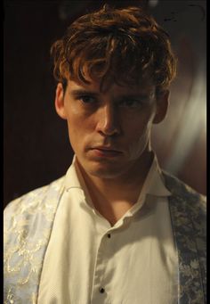 a young man in a white shirt and vest looking at the camera with an intense look on his face