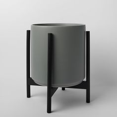 a grey planter sitting on top of a black wooden stand next to a white wall