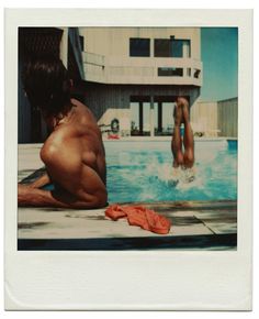 two people are swimming in a pool with towels on the ground and one person has his back to the camera