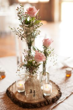 a vase with flowers and candles is on a wooden slice that has been placed on a table