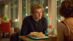 a man sitting at a table with food in front of him and a woman standing next to him