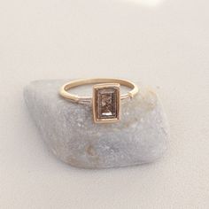 a gold ring with a brown diamond on top of a rock in the middle of a plain white surface