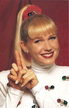 a woman with blonde hair wearing a white shirt and holding her fingers up in the air