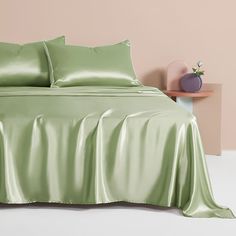 a bed with green sheets and pillows on top of it in front of a pink wall