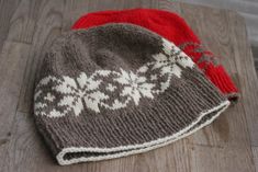 two knitted hats sitting on top of a wooden table next to a red and white object