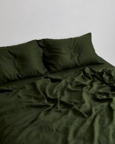 an unmade bed with green sheets and pillows