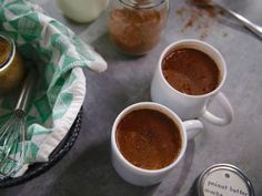 two mugs filled with hot chocolate sitting on top of a table next to jars