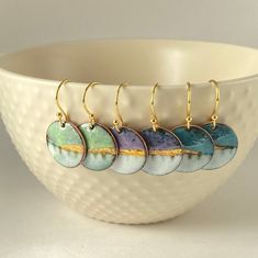 four earrings are hanging from the side of a bowl in front of a white bowl