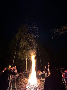 people standing around a fire pit with fireworks in the sky above it at night time