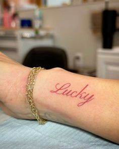 a woman's arm with the word lucky tattooed on her left wrist, in red ink