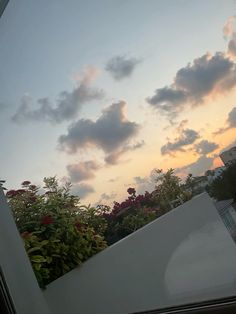 the sun is setting behind some clouds in the sky over trees and bushes on top of a building