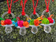 four clear glass vases with colorful flowers hanging from red string and orange ribbons attached to them