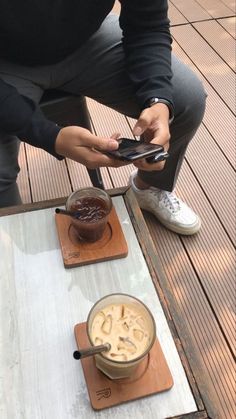 a person sitting on a wooden floor using a cell phone next to a cup of coffee