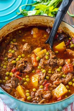 a pot filled with stew and vegetables on top of a blue plate next to a spoon