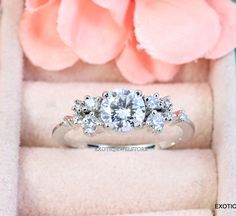 a three stone diamond ring sits in a box next to a pink flower and petals