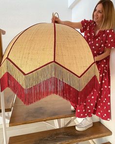 a woman in a red dress is holding up a large piece of straw with fringes on it