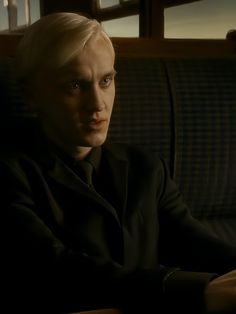 a man with blonde hair sitting on a couch in a dark room looking off into the distance