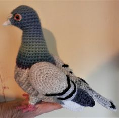 a hand holding a crocheted bird in front of a wall