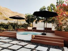 an outdoor hot tub surrounded by wooden steps and umbrellas on the patio with stone pavers flooring