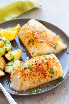 two fish fillets on a plate with potatoes and lemon wedges