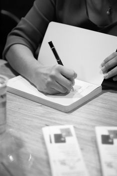 a woman is writing on a notebook with a pen in her hand while sitting at a table