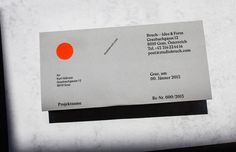 a white and black business card with an orange circle on the front, sitting on top of a piece of paper