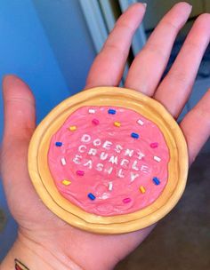 a person's hand holding a pink doughnut with sprinkles on it