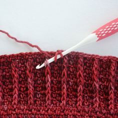 a red knitted object with a white crochet hook