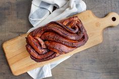 a wooden cutting board topped with sliced up bacon on top of a white cloth next to a knife