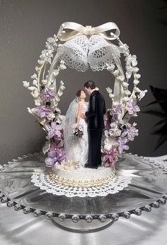 a wedding cake topper with a bride and groom in front of an arch decorated with flowers