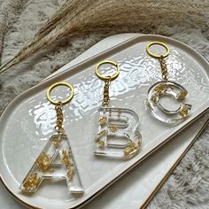 three clear acrylic keychains with gold letters on them sitting on a white platter