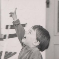 black and white photograph of a young boy pointing at something in the air with his hand