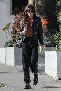 a woman walking down a sidewalk while holding a cup