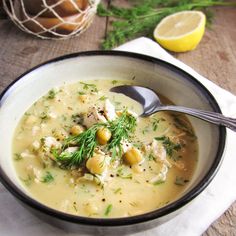 a white bowl filled with soup and garnished with fresh herbs, next to a lemon slice