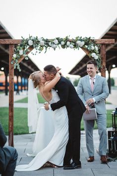 a bride and groom kissing under an arch at their wedding ceremony in front of guests