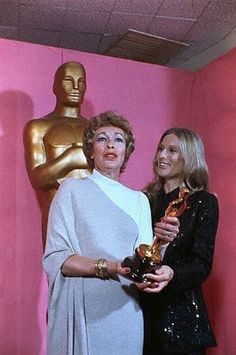 two women standing next to each other in front of a pink wall holding an award