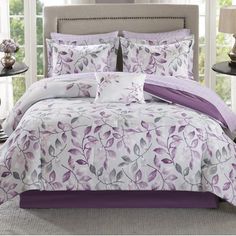 a bed with purple and white comforters in a bedroom next to a lamp on a table