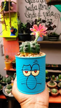 a hand holding a blue tin can with a cartoon face on it and a cactus in the background