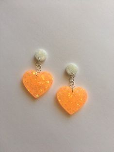 two orange heart shaped earrings with white beads on top of each earring, sitting on a table