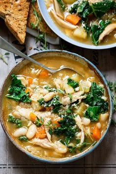 two bowls of chicken and vegetable soup with pita bread on the side next to it