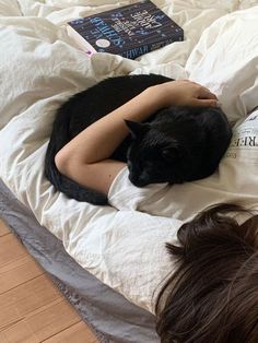 a woman laying on top of a bed with a black cat sleeping next to her