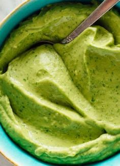 a blue bowl filled with green guacamole and a spoon in the bowl