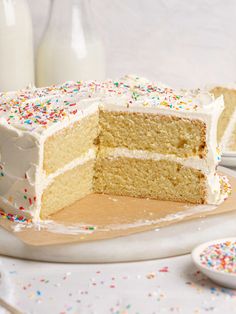 a cake with white frosting and sprinkles sits on a wooden cutting board