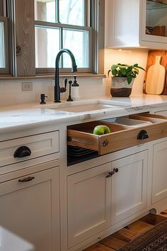 a kitchen sink with an open drawer in the middle and two green apples on top