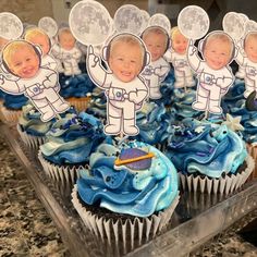 cupcakes with pictures of babies in space are on a clear tray, surrounded by blue frosting