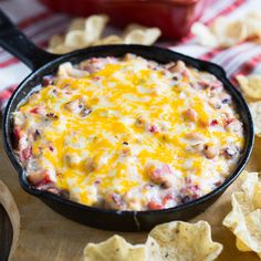 a skillet filled with cheese and chips on top of a wooden cutting board next to a bowl of tortilla chips