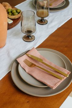 the table is set with plates, silverware and pink napkins for dinner guests