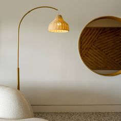 a white chair sitting under a gold lamp next to a round mirror on the wall